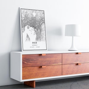 May include: A black and white map print of Oslo, Norway, with the city name and coordinates printed below the map. The print is hanging on a white wall above a white dresser with four drawers. The dresser has a wooden top with copper drawer pulls.