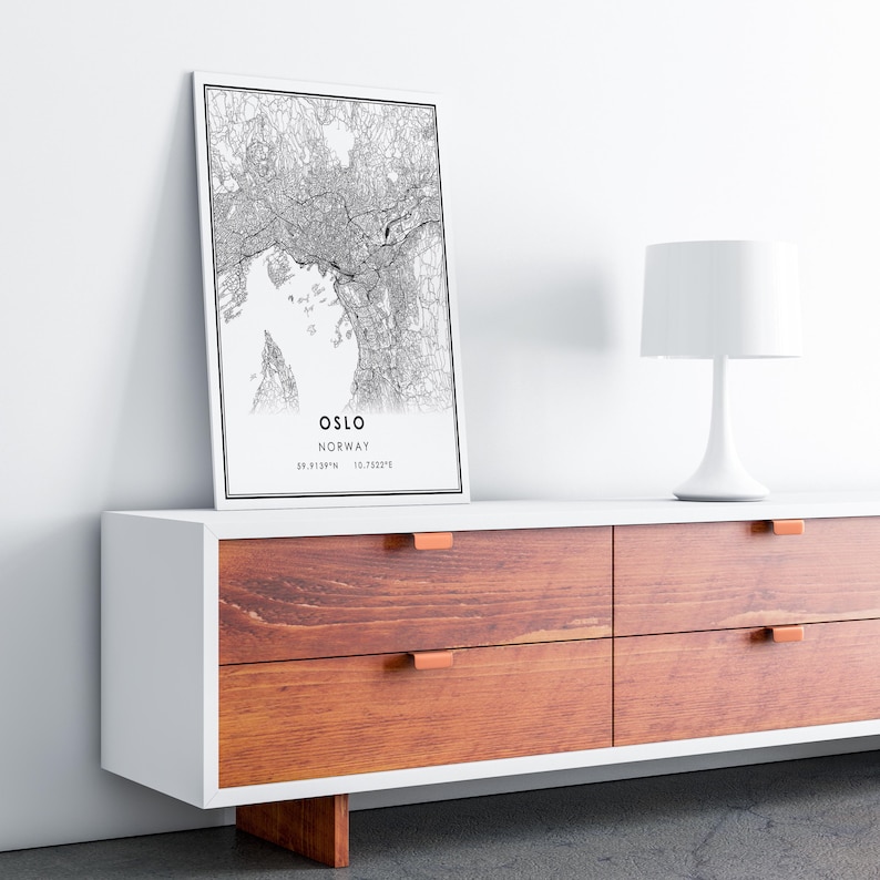 May include: A black and white map print of Oslo, Norway, with the city name and coordinates printed below the map. The print is hanging on a white wall above a white dresser with four drawers. The dresser has a wooden top with copper drawer pulls.