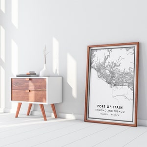 Puede incluir: Una impresi&oacute;n de mapa en blanco y negro enmarcada de Puerto Espa&ntilde;a, Trinidad y Tobago. El mapa est&aacute; rodeado de un marco de madera marr&oacute;n. La impresi&oacute;n est&aacute; en una pared blanca junto a una mesita de noche blanca con dos cajones y patas de color cobre.