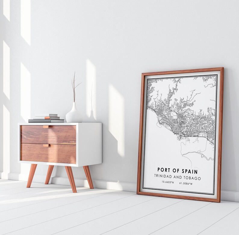 Puede incluir: Una impresi&oacute;n de mapa en blanco y negro enmarcada de Puerto Espa&ntilde;a, Trinidad y Tobago. El mapa est&aacute; rodeado de un marco de madera marr&oacute;n. La impresi&oacute;n est&aacute; en una pared blanca junto a una mesita de noche blanca con dos cajones y patas de color cobre.