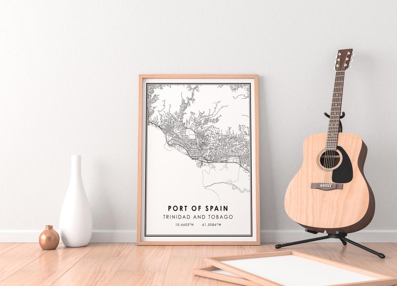 Puede incluir: Una impresi&oacute;n de mapa en blanco y negro de Puerto Espa&ntilde;a, Trinidad y Tobago, enmarcada en un marco de madera clara. El mapa est&aacute; sobre un fondo blanco e incluye las coordenadas 10.6465&deg;N 61.5084&deg;W. La impresi&oacute;n est&aacute; sobre un suelo de madera con un jarr&oacute;n blanco y un jarr&oacute;n marr&oacute;n delante de ella. Una guitarra ac&uacute;stica marr&oacute;n est&aacute; en el fondo.