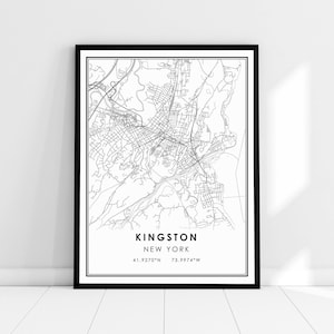 May include: A framed black and white map print of Kingston, New York. The map details the city's streets and surrounding areas. The city name and coordinates are printed at the bottom. The frame is black and the print is displayed against a white wall.