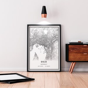 May include: Black and white map print of Oslo, Norway with the city name and coordinates in the bottom right corner. The print is framed in a black frame and hanging on a white wall.