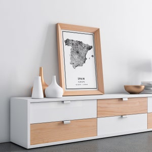 May include: A white dresser with six drawers and wooden accents. A framed black and white map of Spain is on top of the dresser, with the text "SPAIN EUROPE 40.4637&deg; N, 3.7492&deg; W".