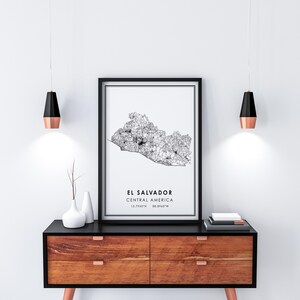 May include: Black and white line art map print of El Salvador, Central America. The print is framed in a black frame and hanging on a white wall above a wooden dresser.