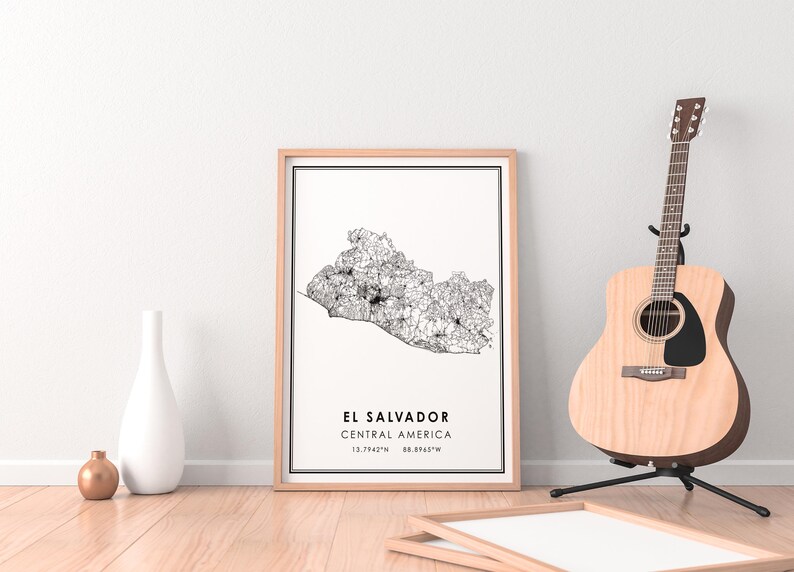 May include: A framed black and white map of El Salvador, Central America with the coordinates 13.7942&deg;N 88.8963&deg;W printed below the map. The map is hanging on a white wall with a wooden floor and a brown acoustic guitar in the background.