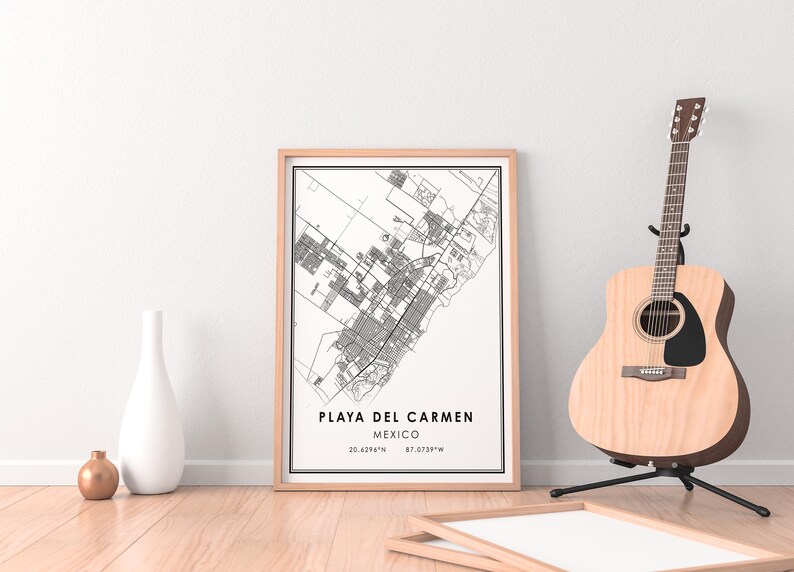 May include: A framed map print of Playa del Carmen, Mexico, in black and white, with coordinates. A wooden acoustic guitar stands on a black stand to the right. A white vase and a small gold vase are on the left.