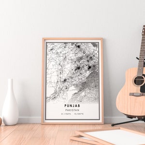 May include: A black and white map print of Punjab, Pakistan, in a light wood frame. The map shows the roads and cities of the region. The print is hanging on a white wall with a wooden floor and a guitar in the background.