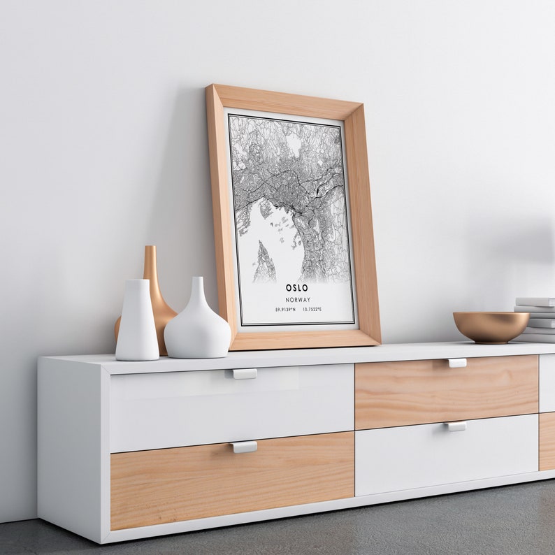May include: A framed black and white map print of Oslo, Norway, with the city name and coordinates printed below the map. The print is hanging above a white and wood dresser with six drawers.
