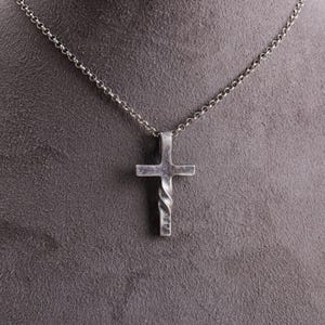 以下が含まれることがあります： シルバーカラーのクロス ペンダント ネックレス。クロスは下部にねじれたデザインがあり、繊細なチェーンから吊り下げられています。 ネックレスはグレーの背景に表示されています。