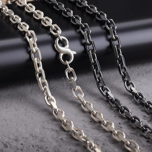 May include: Close-up of three silver chain necklaces with different finishes. One is bright silver, another is oxidized silver, and the third is a darker, gunmetal color. The chains have a classic, elongated link design, with a lobster clasp on one.