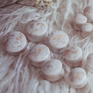May include: A selection of white and gold marble-effect ear plugs and gauges. The plugs are round with a flat face and a slightly rounded edge. The gold accents add a touch of elegance to the jewellery.