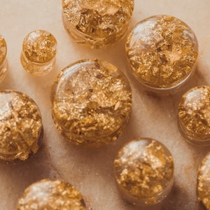 May include: A collection of gold leaf ear gauges in various sizes. The gauges are made of clear acrylic and have a gold leaf design.