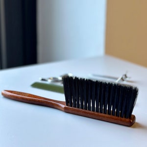May include: A wooden handled brush with black bristles. The brush is on a white surface.