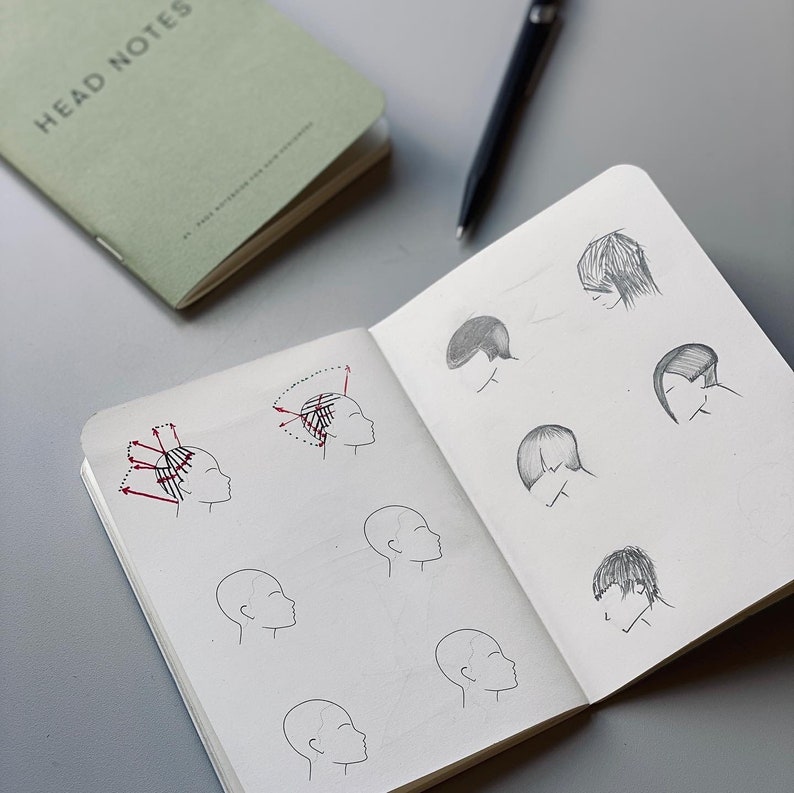 May include: A notebook with a green cover that says "Head Notes" on it. The notebook is open to a page with drawings of different hairstyles. The drawings are in pencil and show different haircuts and hair lengths. The page also includes a diagram of a head with arrows showing the direction of hair growth.