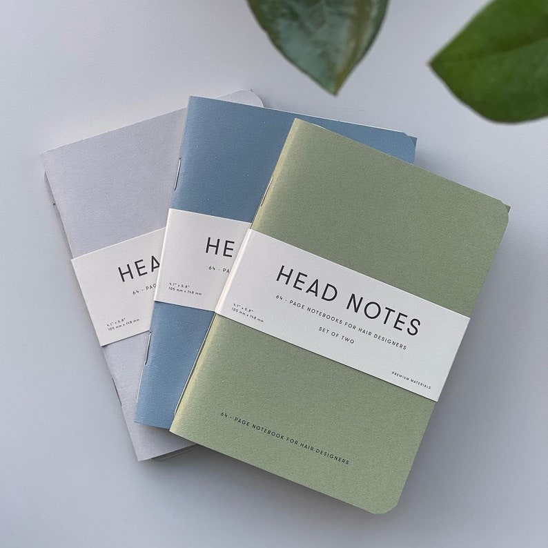 May include: A set of two 64-page notebooks for hair designers. The notebooks are green, blue, and gray. The cover of the green notebook says "Head Notes 64-Page Notebooks for Hair Designers Set of Two Premium Materials 64-Page Notebook for Hair Designers".