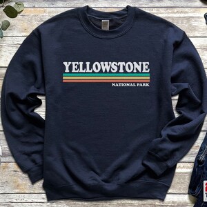 May include: Navy blue sweatshirt with a white graphic that says "Yellowstone National Park" with a green, orange, and brown stripe design.