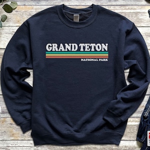 May include: Navy blue sweatshirt with a white graphic that says "Grand Teton National Park" with colorful stripes.
