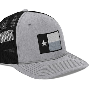 May include: A gray and black trucker hat with a black and white embroidered Texas flag on the front.