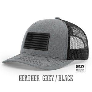May include: Heather grey trucker hat with a black American flag patch and black mesh back. 207 Threads.
