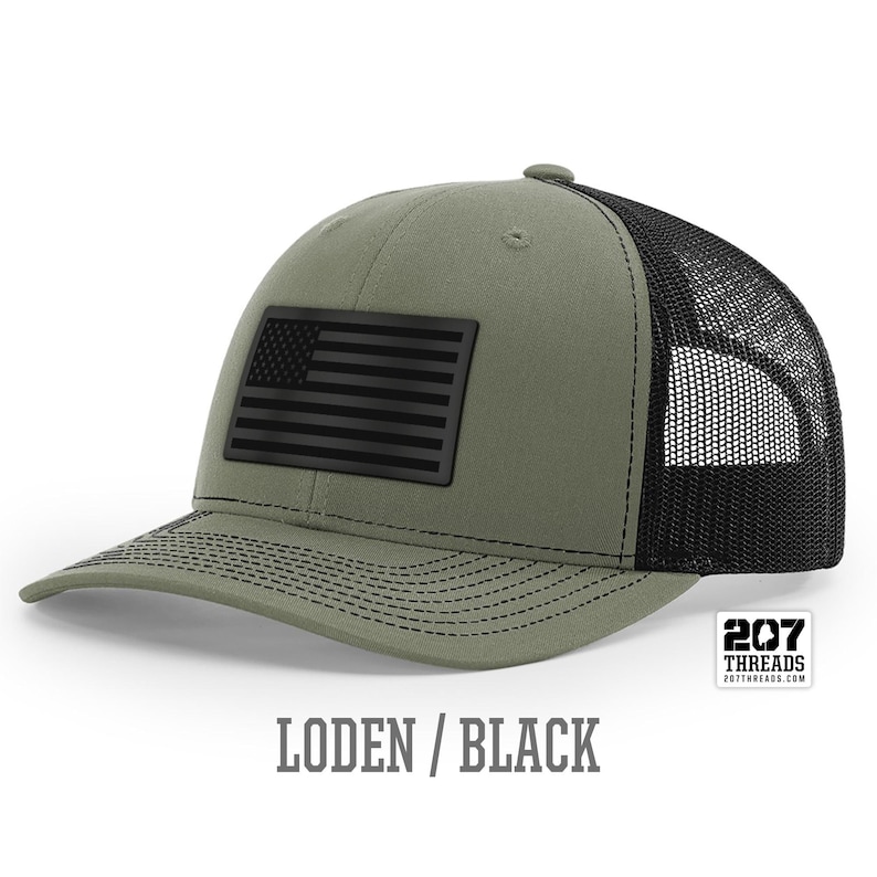 May include: A green and black trucker hat with a black American flag patch. The hat has a mesh back and is labeled "207 Threads".