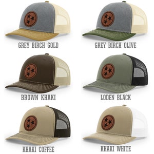 May include: Five different color combinations of a trucker hat with a brown leather patch featuring the three stars of the Tennessee state flag. The hat colors are grey birch gold, grey birch olive, brown khaki, khaki coffee, and khaki white.