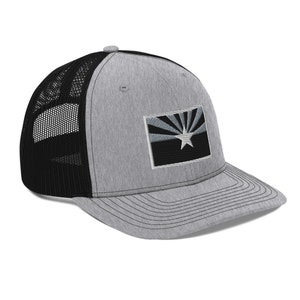 Puede incluir: Una gorra de camionero gris y negra con un parche negro que muestra la bandera del estado de Arizona. La bandera está bordada en blanco con una estrella blanca en el centro.