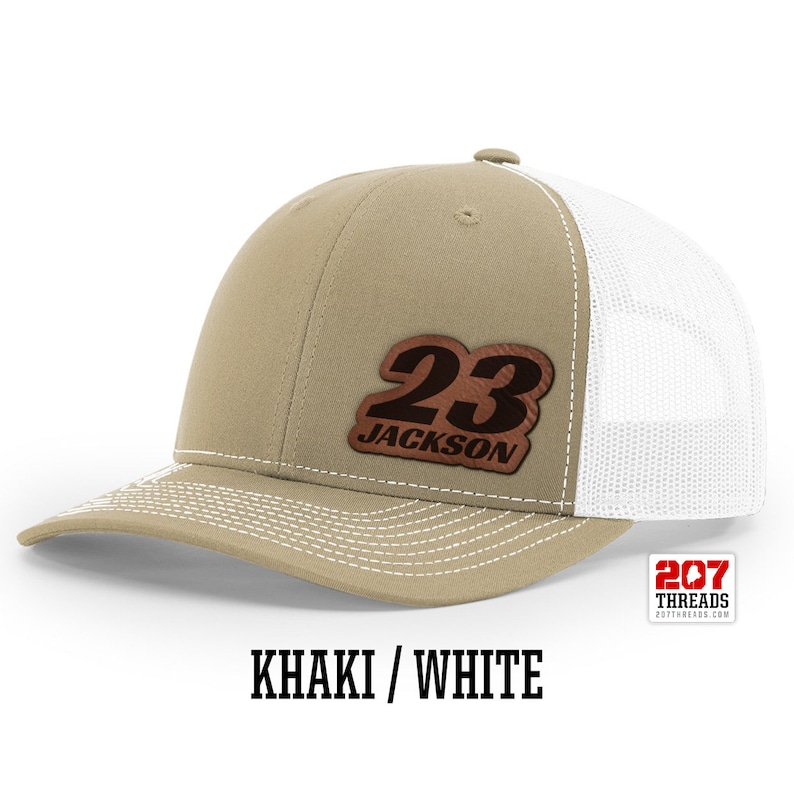 May include: Khaki and white trucker hat with a brown leather patch that says "23 JACKSON" on it.