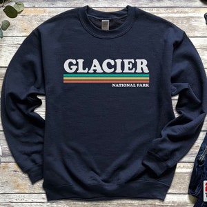 May include: Navy blue sweatshirt with a white graphic of the text "GLACIER NATIONAL PARK" in a retro style with colorful stripes.