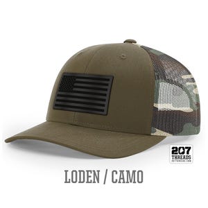 May include: A green and camo trucker hat with a black American flag patch on the front. The hat has a mesh back and the text "207 Threads" is on the back.