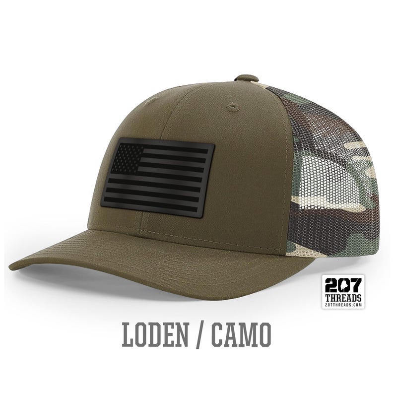 May include: A green and camo trucker hat with a black American flag patch on the front. The hat has a mesh back and the text "207 Threads" is on the back.