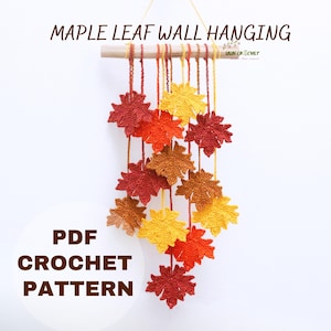 Puede incluir: Un colgante de pared de hojas de arce de ganchillo en colores otoñales. Las hojas son en tonos de rojo, naranja y amarillo, suspendidas de una clavija de madera. El texto "MAPLE LEAF WALL HANGING" y "PDF CROCHET PATTERN" son visibles.