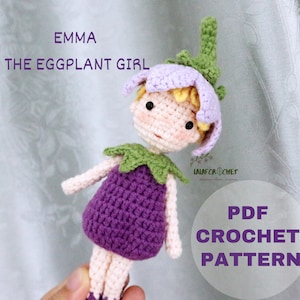 Puede incluir: Patrón de crochet para una muñeca de niña de berenjena morada llamada Emma. La muñeca tiene un tallo y hojas verdes, y un vestido morado. El patrón está disponible para descargar en PDF.