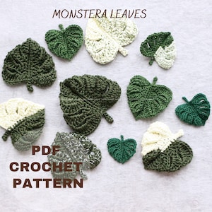 May include: A set of crochet monstera leaves in various shades of green and white. The leaves are arranged on a light grey fabric background. The text "PDF CROCHET PATTERN" is printed in black on the fabric.