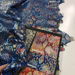 May include: Close-up of a sample swatch book of metallic snakeskin fabric in red, blue, and orange. The fabric has a iridescent sheen.