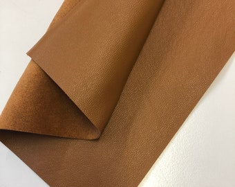 May include: A close-up of a brown faux leather fabric with a textured surface. The fabric is folded in half, showing both the front and back sides.