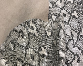 May include: A close-up of a white and black snakeskin fabric with a textured pattern. The fabric is folded and has a smooth, light brown backing.