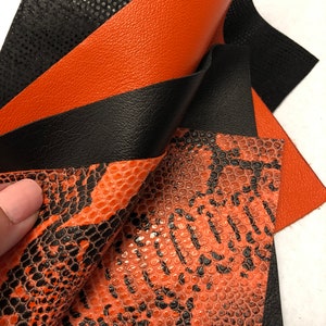 May include: Close-up of three pieces of orange and black faux leather. The leather has a textured, snake-like pattern.