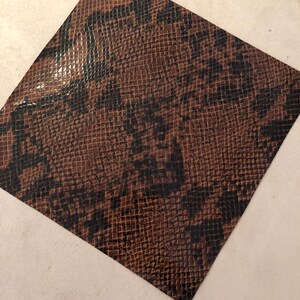 May include: A close-up of a brown snakeskin-patterned fabric with a glossy finish.