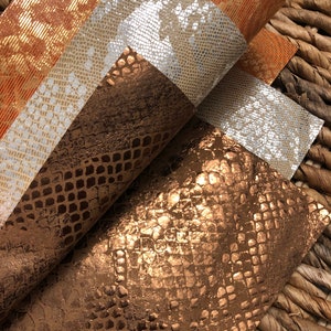 May include: Three pieces of faux leather fabric with a snakeskin pattern. The fabric is in shades of brown, gold, and silver.