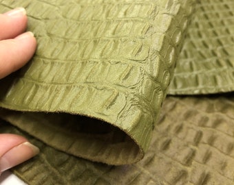 May include: Close-up of a green textured fabric with a crocodile skin pattern. The fabric is folded in half, showing the texture on both sides.
