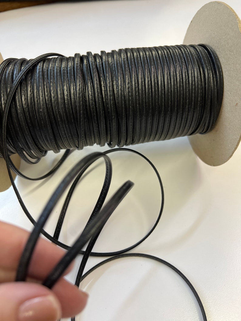 May include: A spool of black leather cord, wound around a cardboard core. The cord is smooth and has a slight sheen.
