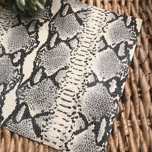 May include: A sheet of faux snakeskin fabric with a white background and a black and gray snake skin pattern.