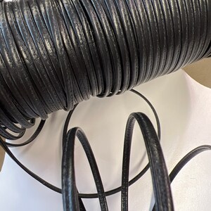 May include: A spool of black leather cord. The cord is wound tightly around the spool and is about 1/4 inch wide.