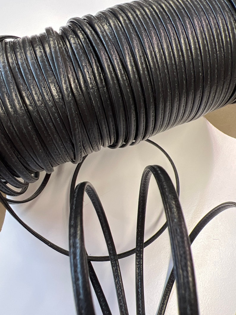 May include: A spool of black leather cord. The cord is wound tightly around the spool and is about 1/4 inch wide.
