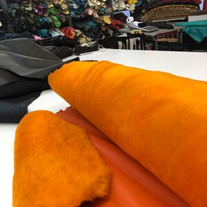 May include: A roll of orange faux fur fabric with a piece of orange leather next to it.