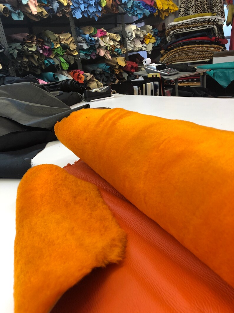 May include: A roll of orange faux fur fabric with a piece of orange leather next to it.