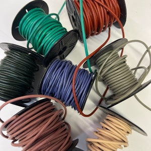 May include: Spools of leather cord in various colors, including green, brown, gray, purple, and beige. The cords are wound around spools with black plastic bases.