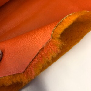 May include: Close-up of a piece of orange faux leather with a fuzzy orange lining. The leather is folded over to show the lining.