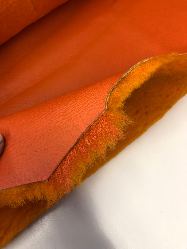 May include: Close-up of a piece of orange faux leather with a fuzzy orange lining. The leather is folded over to show the lining.